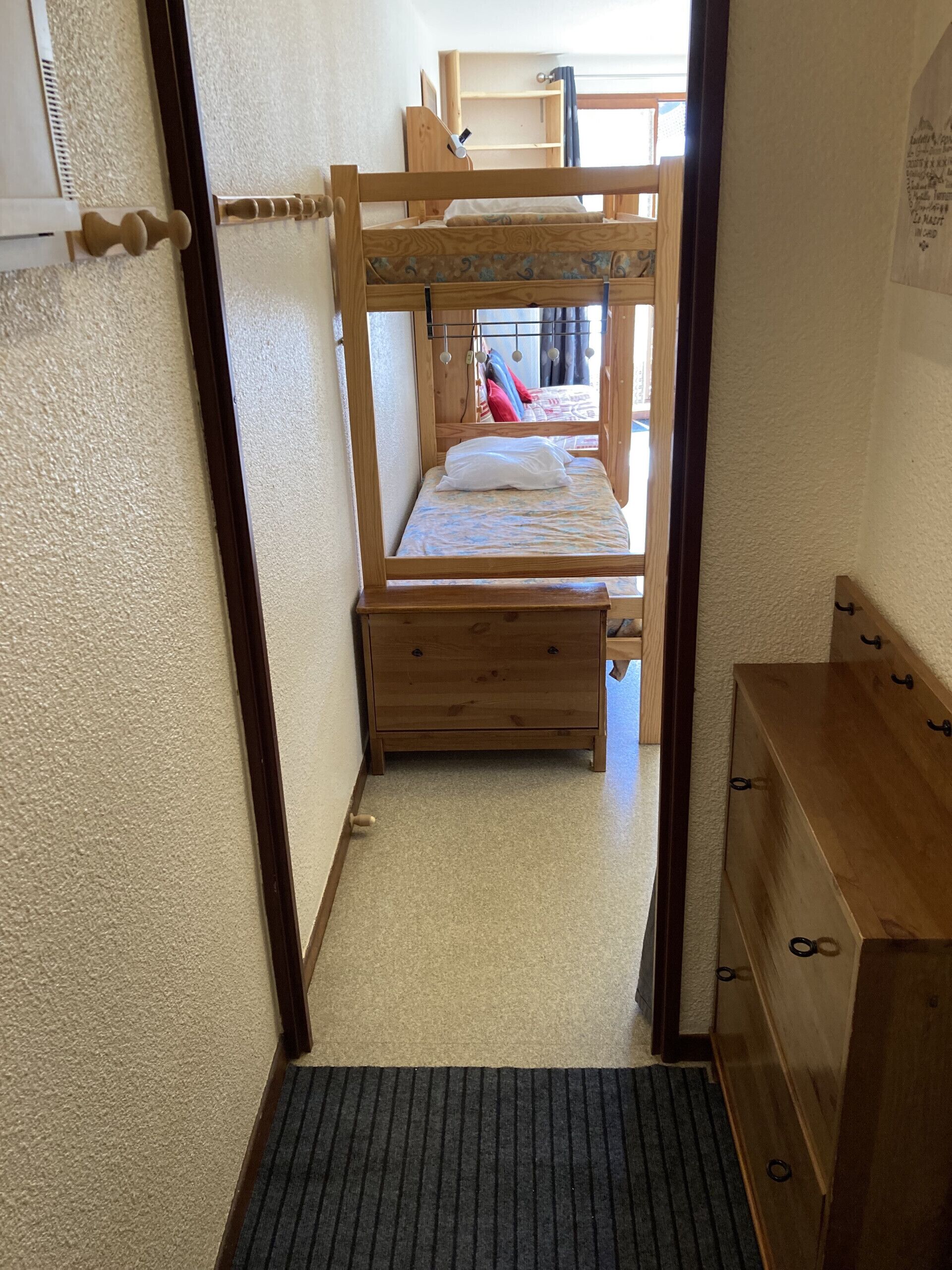 Een smalle gang die uitkomt in een slaapkamer met stapelbedden, een houten dressoir en een klein bureau.