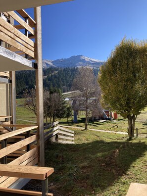 A wooden deck with a view of a mountain and a tree in the foreground. - Appartement N°29 au Griou (Le Lioran)