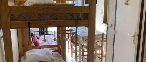 A bunk bed with a wooden frame and a lower drawer, a desk, and a chair in the background.