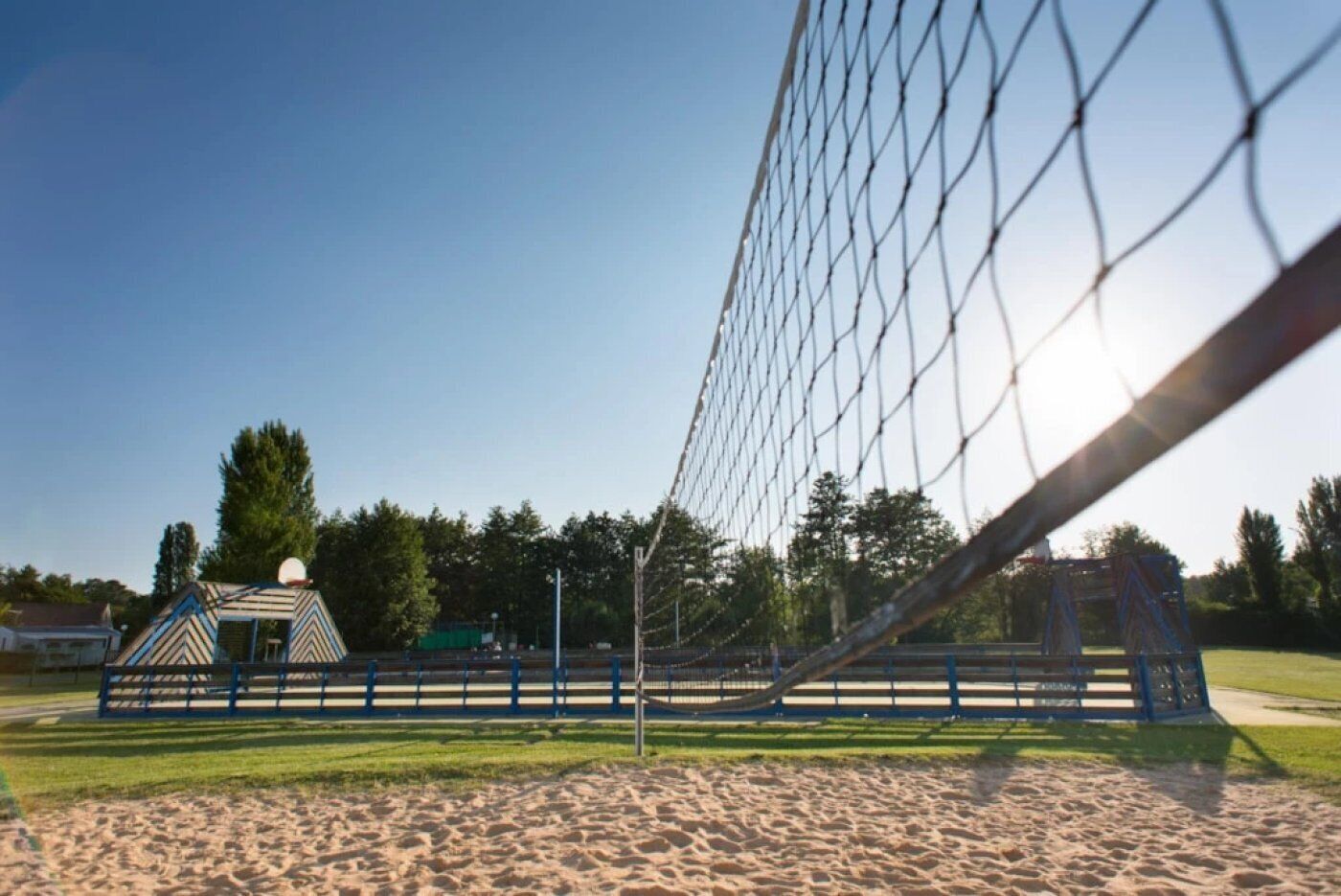 Zona de playa con arena, una red de voleibol, un pequeño pabellón y un parque infantil.