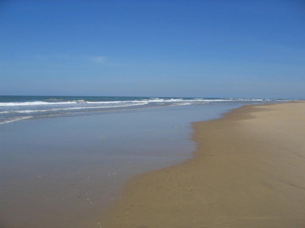 Une vaste plage de sable fin, avec des vagues douces et un ciel dégagé.