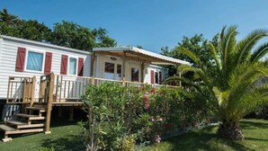 A mobile home with a porch and a small garden area with palm trees and flowering plants. - ZEcamping 4 étoiles familial toboggans 1km plage locatif clim 28m2 (Valras-Plage)