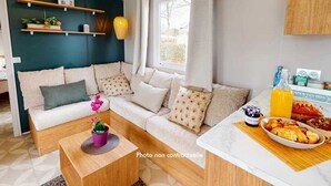 A modern living room with a sofa, coffee table, and a breakfast bar with food items. - ZEcamping 4* 1km plage toboggans pet friendly animations locatif 36m2 (Les Mathes)