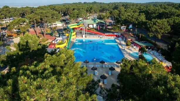 A large swimming pool with a water slide, surrounded by trees and a small building. - ZEcamping 4* 1km plage toboggans pet friendly animations locatif 36m2 (Les Mathes)