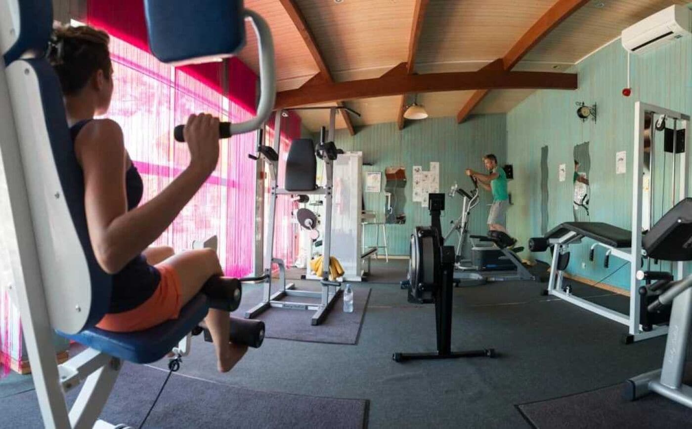Une salle de sport équipée de divers appareils, notamment un rameur, un tapis de course et un vélo d’appartement.