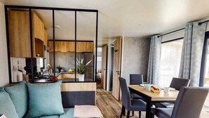 Un salon moderne comprenant un canapé, une table à manger, des chaises et un coin cuisine visible à travers une cloison en verre.