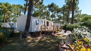 A mobile home with a deck, surrounded by trees and a grassy area. - ZEcamping 4* 1km plage toboggans dog friendly locatif clim 36m2 8 pers (Les Mathes)