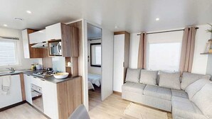 A compact RV interior with a kitchenette, a sofa, and a bed. - ZEcamping 4* 1km plage toboggans dog friendly locatif clim 36m2 8 pers (Les Mathes)