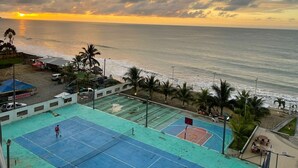 Vista costera con cancha de baloncesto, playa y palmeras.