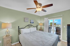A bedroom with a bed, ceiling fan, two bedside lamps, a nightstand, a window with a view of the ocean, and a balcony with a chair. - 🌊Across the Street from Beach | Gulf Views | Grand Caribbean 209🌊 (Orange Beach)
