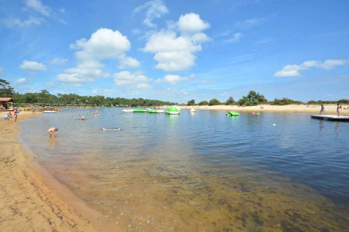 A beach with clear water, people swimming, and boats.