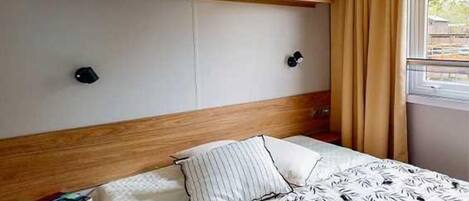 A bedroom with a bed, wooden headboard, two wall-mounted lights, and a window with curtains.