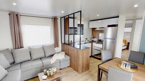 A modern living room with a sofa, a dining table, and a kitchen area with a refrigerator and stove.