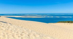 Ein Sandstrand mit klarem, blauen Wasser und weiter Landpartie im Hintergrund.
