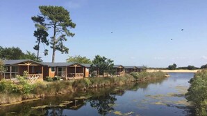 A row of cabins by a calm lake with reflections, surrounded by natural vegetation.