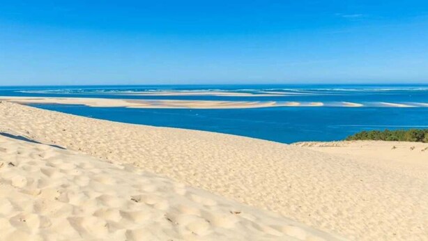 Eine Wüstenlandschaft mit Sanddünen und Blick auf den Ozean.