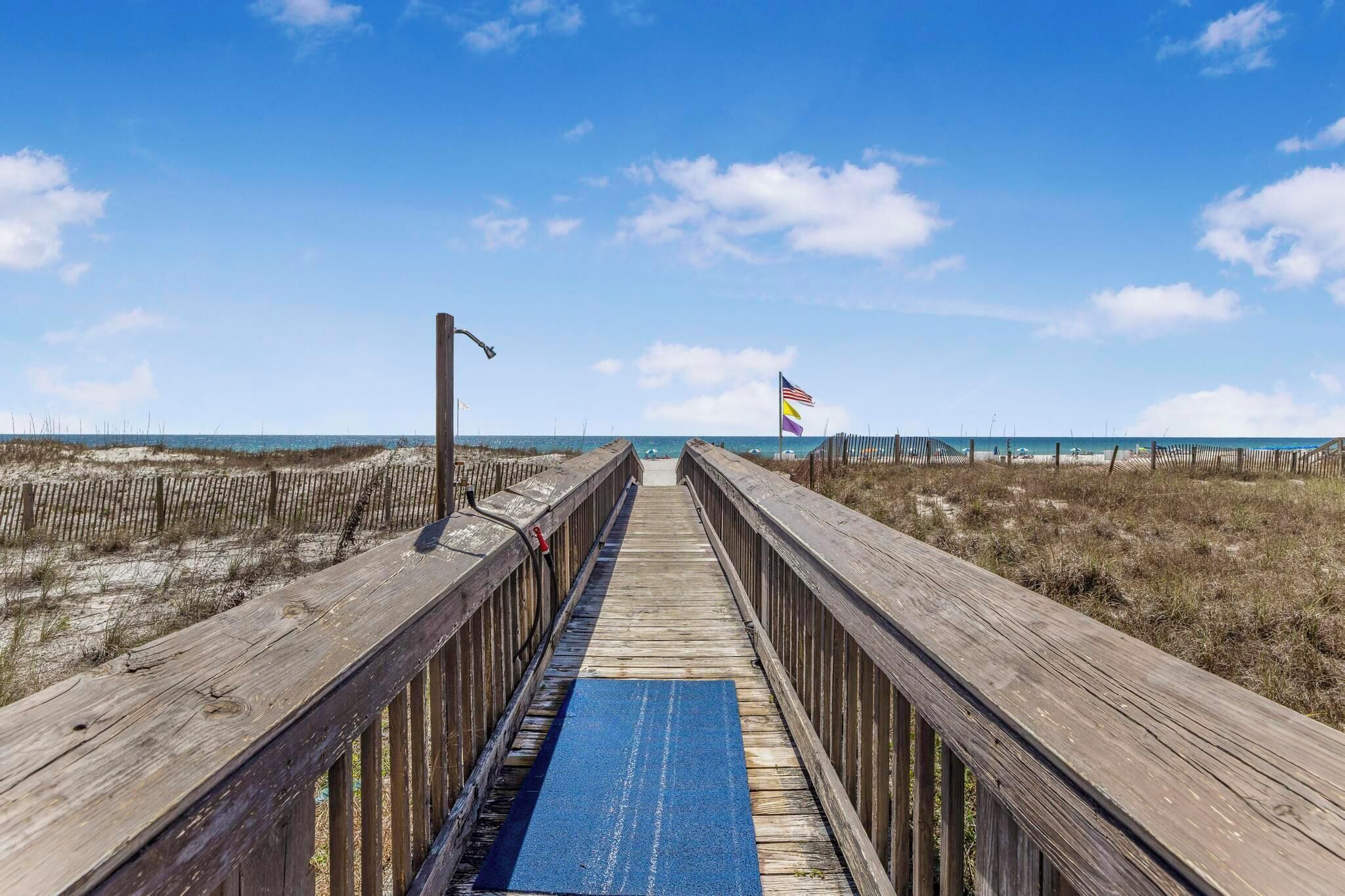 Un paseo marítimo de madera que lleva a la playa, con una bandera a lo lejos.