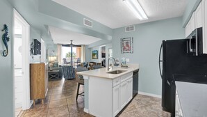 A spacious kitchen with a large island, white cabinetry, and a black refrigerator. - 🌞Beachfront Condo with Indoor & Outdoor Pools | Harbour Place 109🌞 (Orange Beach)