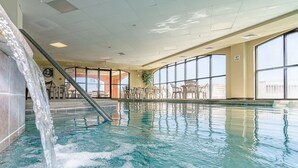 An indoor swimming pool with clear water, a waterfall feature, and large windows offering views of the outside. - 🌞Beachfront Condo with Indoor & Outdoor Pools | Harbour Place 109🌞 (Orange Beach)
