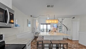 Ett modernt kök med en stor köksö, barstolar, en inbyggd ugn och utsikt mot omgivningen.
