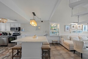 Une cuisine moderne avec des meubles blancs, un îlot central et un coin repas comprenant un canapé et des chaises blancs.