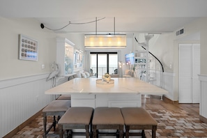 Une cuisine spacieuse dotée d’un grand îlot central, de luminaires suspendus et offrant une vue sur l’extérieur.