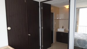 A bedroom with a bed, a bedside table, a wardrobe, and a bathroom with a sink and mirror. - Lucille's Corner (Carolina)