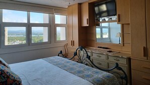A bedroom with a bed, a ceiling fan, a TV, wooden cabinets, and a window with a view of a landscape. - Lady From Spain (Carolina)