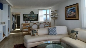 A living room with a beige sofa, a glass coffee table, and a dining area with a wooden table and chairs. - Lady From Spain (Carolina)