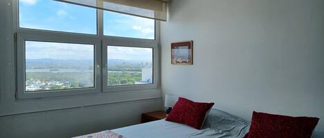 A bedroom with a bed, two red pillows, a nightstand, a lamp, and a framed picture on the wall.