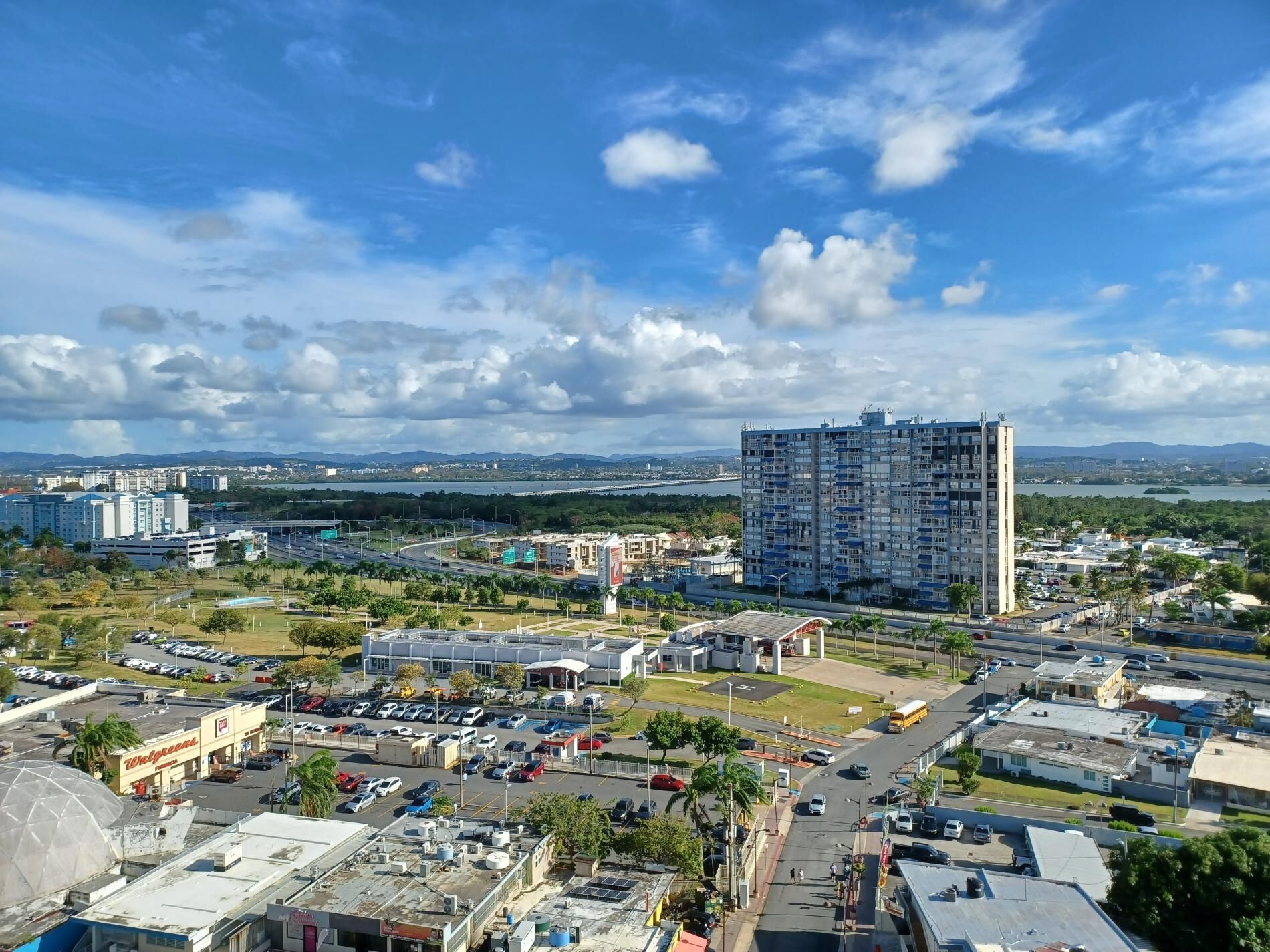 A cityscape with a large building, parking lots, and a clear sky.