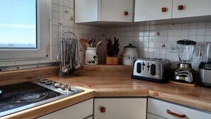 A kitchen with white cabinets, a wooden countertop, a stove, a toaster, a blender, and a window with a view of the sea. - Lady From Spain (Carolina)