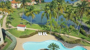 A resort with a swimming pool, palm trees, and a lake.
