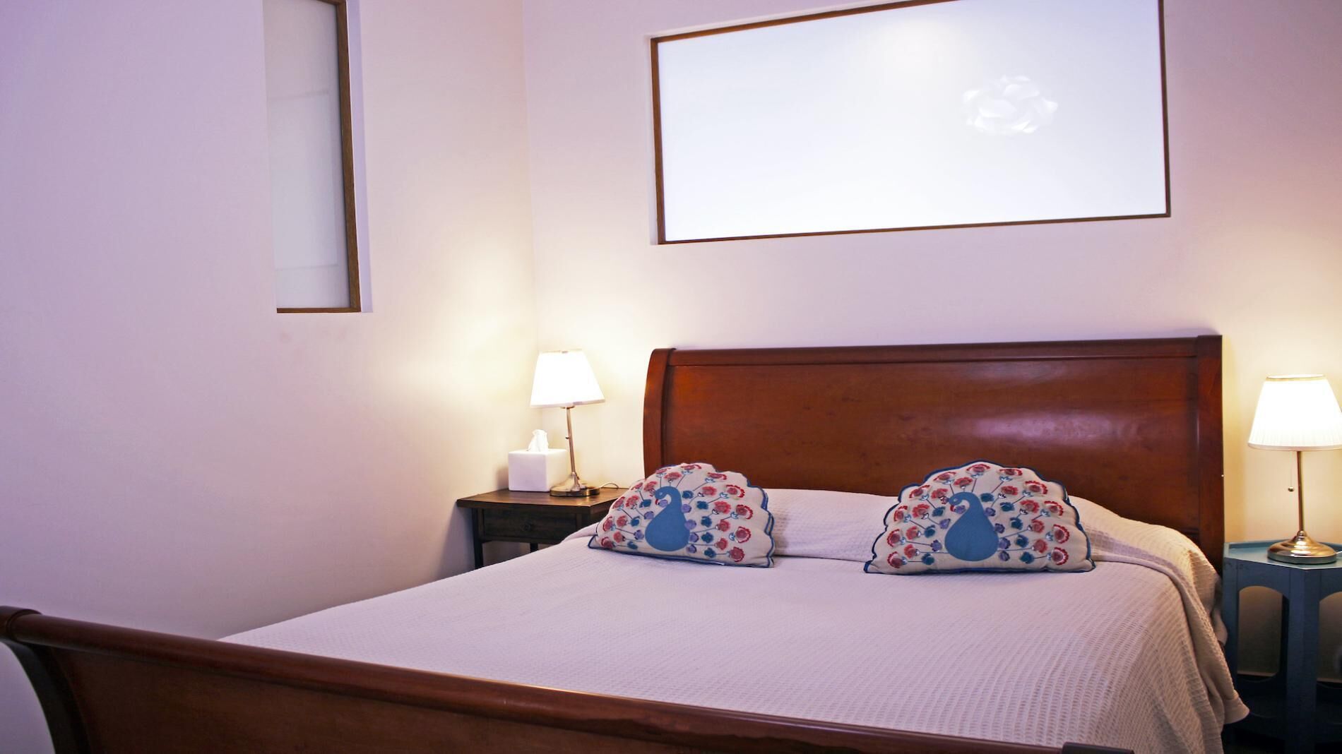 Una cama bien hecha con cabecera de madera, dos lámparas de noche y un cuadro enmarcado en la pared.
