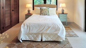 A bedroom with a large bed, two bedside tables with lamps, a window with a view of greenery, and a wooden wardrobe. - Orchid Villa (Río Grande)