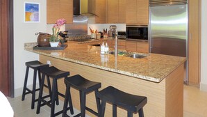 A modern kitchen with a granite countertop, stainless steel appliances, wooden cabinets, and bar stools. - Orchid Villa (Río Grande)
