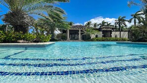 A clear swimming pool with blue tiles, surrounded by palm trees and a building with a tiled roof.