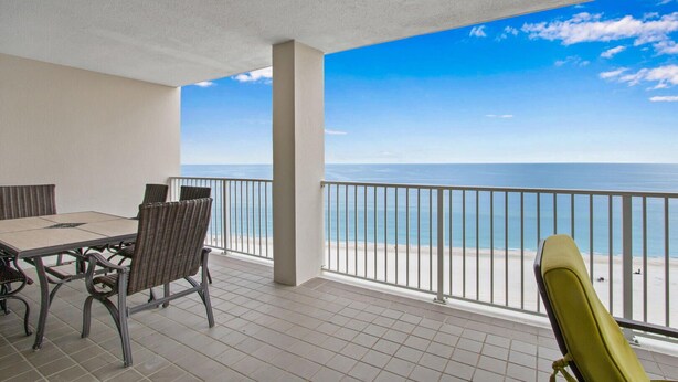 Een balkon met uitzicht op zee, een tafel met stoelen en een hekwerk.