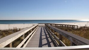 Een houten looppad dat naar een strand leidt, onder een heldere lucht.
