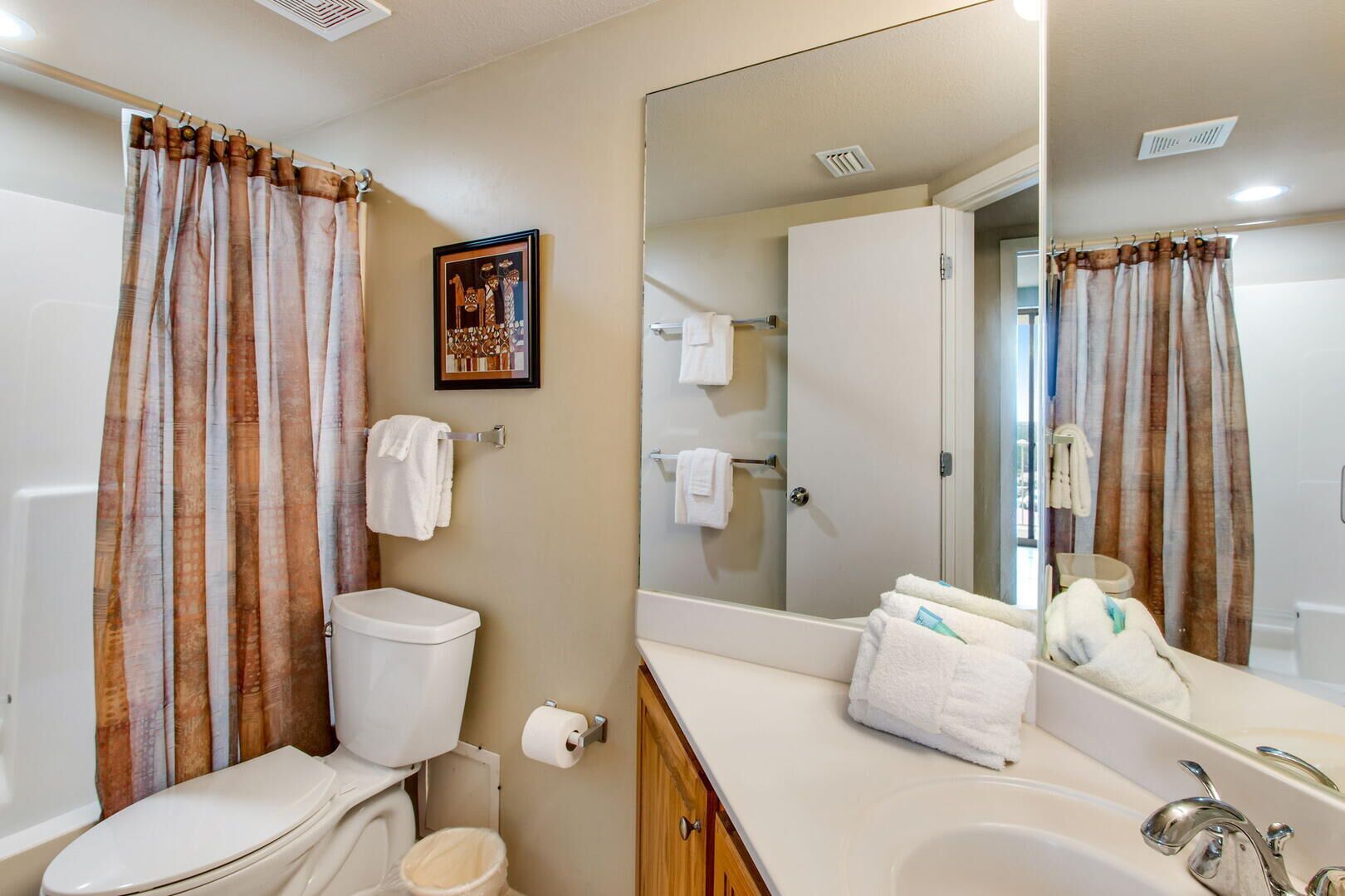 Une salle de bain avec des toilettes, un lavabo et un miroir. On y trouve des serviettes et un tableau encadré accroché au mur.