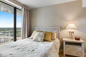 Een slaapkamer met een groot bed, een nachtkastje met een lamp en een uitzicht op een stadsgezicht vanaf een balkon.