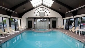 Una piscina interior con paredes de vidrio transparente, tragaluz y sillones de descanso.
