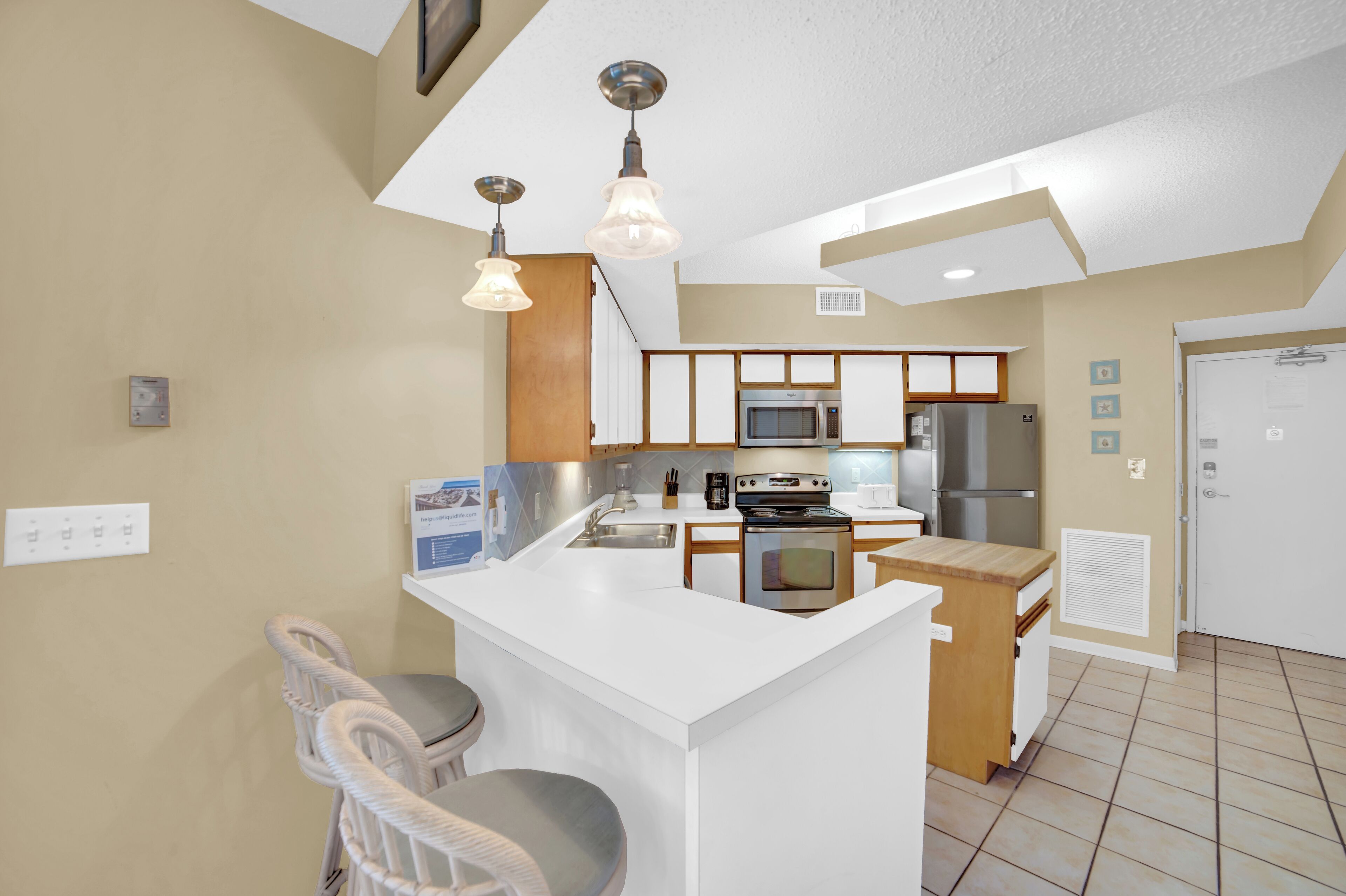 A compact kitchen with a central island, built-in microwave, refrigerator, and a small seating area with chairs.