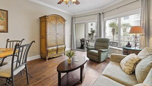 A living room with a wooden floor, a sofa, a chair, a table, a cabinet, and a ceiling fan. - ⭐Outdoor Pool | Gulf and Pool Views | Palm Beach A23⭐ (Orange Beach)
