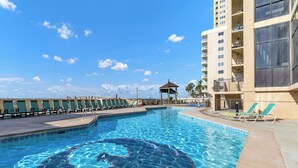 A swimming pool with lounge chairs and a gazebo, surrounded by a tall building with balconies. - 🌞Beachfront Bliss | Gulf Views | Amazing Amenities | Phoenix I 1097🌞 (Orange Beach)