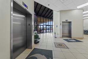 Una hall moderna e pulita con due ascensori, una vista aperta sull'esterno tramite ampie finestre e un pavimento piastrellato con tappetino d'ingresso.