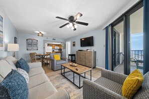 A spacious living room with a ceiling fan, a dining area, and a kitchen in the background.
