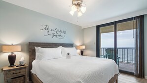 Ein Schlafzimmer mit einem Bett, zwei Nachttischlampen, einem Nachttisch, einem Wandspruch und einem Balkon mit Blick.
