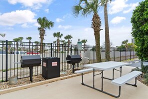 Een picknicktafel met een bank, een barbecue en afvalbakken.