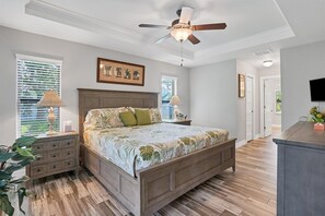 Cozy bedroom with a central bed, nightstand, dresser, and television, featuring a floral-patterned bedspread and a framed picture.